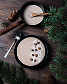 From above of black bowls with cream soup of chestnuts placed on wooden table with green branches of fir with cones