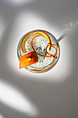 Top view of transparent glass of highball cocktail decorated with citrus fruit zest and clove against shadows in sunlight