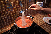 Von oben von Ernte weiblich Hinzufügen von Salz in Topf beim Kochen Marinara-Sauce aus Tomaten auf dem Herd in der Küche