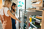 Anonyme weibliche Person in Interaktion mit einem Partner, während sie leckere Torten hinter einer Vitrine in einer Konditorei zeigt