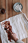 Top view of unrecognizable person spreading tasty fig jam on thin pastry dough with cream cheese on timber table