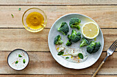 Draufsicht auf leckeren Brokkoli mit frischer Zitrone und Sauce neben Schalen mit Olivenöl und Gewürzmischung auf Holztisch