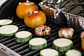 Closeup raw slices of fresh zucchini and garlic heads with tomatoes grilling on metal grate