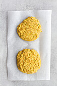 Top view of raw homemade veggie chickpea and curry cutlets in bread crumbs for burger on parchment sheet on gray background