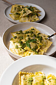 Appetizing cooked ravioli pasta with green sauce and herbs placed on white plates with forks on table
