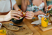 Crop best female friends sitting at wooden table with tasty croissants and beverages in cafeteria