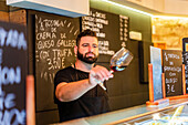 Unscharfer Barmann mit steriler Maske steht an der Theke und schaut in ein Weinglas, während er in einem Restaurant arbeitet