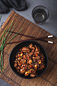 From above of bowl with Asian chicken with almonds and vegetables placed near bamboo chopsticks and chives