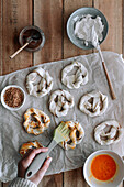 Top view of unrecognizable person spreading raw egg on pretzels with fig jam and cream cheese on timber table