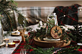 Christmas table setting with wreath on the plate, decorative wooden ornaments and red checkered tablecloth with yellow lights on the background