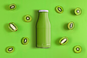 Top view of bottle of fresh juice of green color place on background with halves of ripe kiwi