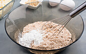 Glasschüssel mit Mehl und Backpulver zum Backen kohlenhydratarmer Bagels mit Schneebesen auf einem Tisch mit Zutaten in der Küche