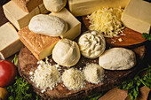 Collection of Italian cheese on table with fresh vegetables and curly parsley with basil leaves on spatulas