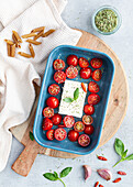 Top view of ripe cherry tomatoes with black olive slices and feta cheese in baking dish near uncooked penne