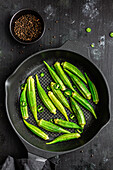 From above ripped fresh okra on frying pan with green pepper on dark background