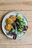Top view of plate of sweet potato falafel and lettuce salad served with lime on wooden table