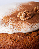 Close-up of tasty carrot cake piece with walnut and cinnamon powder on icing sugar glaze on light background