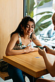 Best female friends surfing internet on cellphone while talking at cafeteria table in daylight