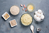 Draufsicht auf verschiedene Zutaten für Brot mit zerkleinertem Blumenkohl in der Nähe von Eiern, die auf dem Tisch neben Gewürzen und Semmelbröseln mit Mehl und geschmolzener Butter liegen
