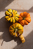 From above of ripe whole pumpkins with cite slice placed on beige marble table on sunny day in kitchen