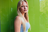 Seitenansicht einer Millennial-Frau mit blondem Haar, die der Kamera auf grünem Hintergrund zuzwinkert