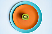 Blick von oben auf die Hälfte einer frischen, reifen, saftigen Kiwi auf einem orangefarbenen und blauen Teller auf weißem Untergrund