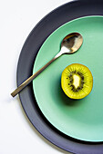 From above of half of fresh ripe juicy kiwi and spoon placed on grey and green plates on white surface