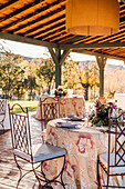 Geräumige Veranda mit Tellern, Weingläsern und Besteck auf mit frischen Blumen geschmückten Tischen für eine Hochzeitsfeier