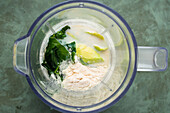 Draufsicht auf eine Mixerschüssel mit frischem Spinat, der mit Proteinpulver und Milch für die Zubereitung eines grünen Keto-Diät-Smoothies zerkleinert wurde