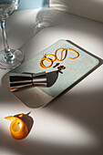 Blick von oben auf ein Glas in der Nähe eines Metallgefäßes mit Zitrusfruchtschalen und trockenen Gewürzen auf einem Tisch mit Schatten