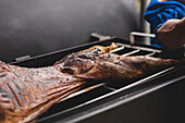 Crop faceless cook with grilling lamb on metal rack during cooking process