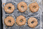 Top view of uncooked low carbohydrate bagels sprinkled with sesame seeds placed on baking paper on tray in light kitchen
