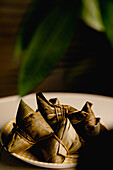 Geöffnete und bedeckte Bambusblatt-Reisknödel auf einem hübschen karierten Teller