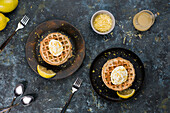 Stapel von leckeren hausgemachten süßen gebackenen Chaffeln auf schwarzem Teller mit Zitrone und Schale auf Tisch in heller Küche