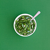 Gesunder Salat mit grünen Bohnen und Knoblauchscheiben in einer Schüssel auf einem grünen Tisch, von oben betrachtet