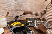 Crop anonymous ethnic person frying cooking banana pieces in pan with hot oil on stove while preparing patacones in kitchen