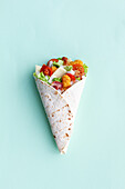 Top view of delicious chicken wrap with fresh lettuce and ripe tomatoes in tortilla placed on light background in studio