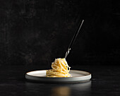 Spaghetti mit geriebenem Käse um eine Gabel gewickelt isoliert auf einem modernen Teller auf einem dunklen Hintergrund