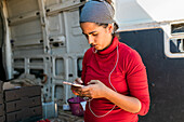 Concentrated female gardener in bandana browsing cellphone while working in farm and looking at screen