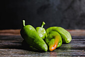 Fresh green peppers with various shapes on smooth lumber table in rustic kitchen