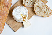 Von oben köstlicher Camembert-Käse auf hölzernem Schneidebrett neben Brotscheiben auf weißem Hintergrund