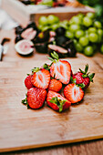Reife köstliche Erdbeeren vor Feigen und Weintrauben auf einem Holzbrett auf dem Tisch