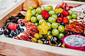 Fleischdelikatessen neben einem Haufen mit Früchten und Beeren in einer Holzkiste auf einem Tisch