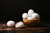 Uncooked eggs in bowl placed on wooden table in dark background for cooking breakfast