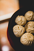 Overhead crop view of hot delicious steamed xiaolongbao in bamboo basket on table in Asian restaurant kitchen