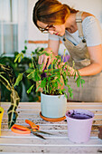 Young female florist in apron planting green plant into ceramic pot while working in professional floristry studio