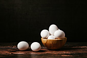 Ungekochte Eier in einer Schale auf einem Holztisch vor dunklem Hintergrund zum Frühstück