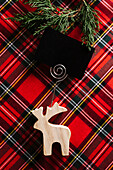 Christmas Reindeer of wood with blank name card on red checkered fabric and decorative pine wreath.