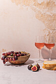 Glasses of red drink placed on table with bowl of grapes and figs near baguette slices