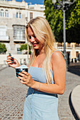Schöne blonde junge Frau isst kaltes leckeres Eis, während sie an einem sonnigen Sommertag auf der Straße steht